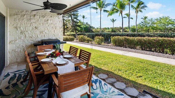 An outdoor dining area with a table set for four, a ceiling fan, and a view of a well-manicured lawn and palm trees. - Keauhou Punahele E103, w/AC (Kailua Kona)