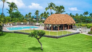 A pool area with a thatched-roof gazebo, surrounded by palm trees and a well-maintained lawn. - Keauhou Punahele E103, w/AC (Kailua Kona)