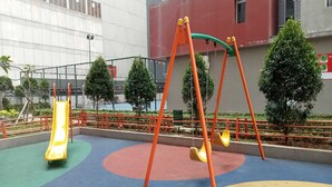 A playground with a slide and swings, surrounded by a fence and trees. - OYO LIFE ROOMS BY MIXO  (Jakarta)