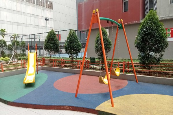 A playground with a slide and swings, surrounded by a fence and trees. - OYO LIFE ROOMS BY MIXO (Jakarta)