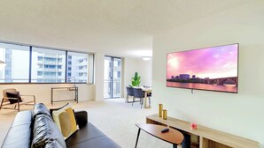 Uma sala de estar moderna com uma janela grande, um sofá, um espaço de refeições e uma TV de tela plana na parede.
