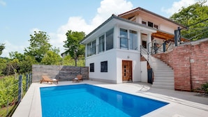 Une maison moderne à deux étages, dotée d’une piscine, d’une terrasse en bois et d’un escalier en briques.