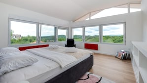 Une chambre moderne avec un grand lit, de nombreuses fenêtres et une vue sur la verdure.
