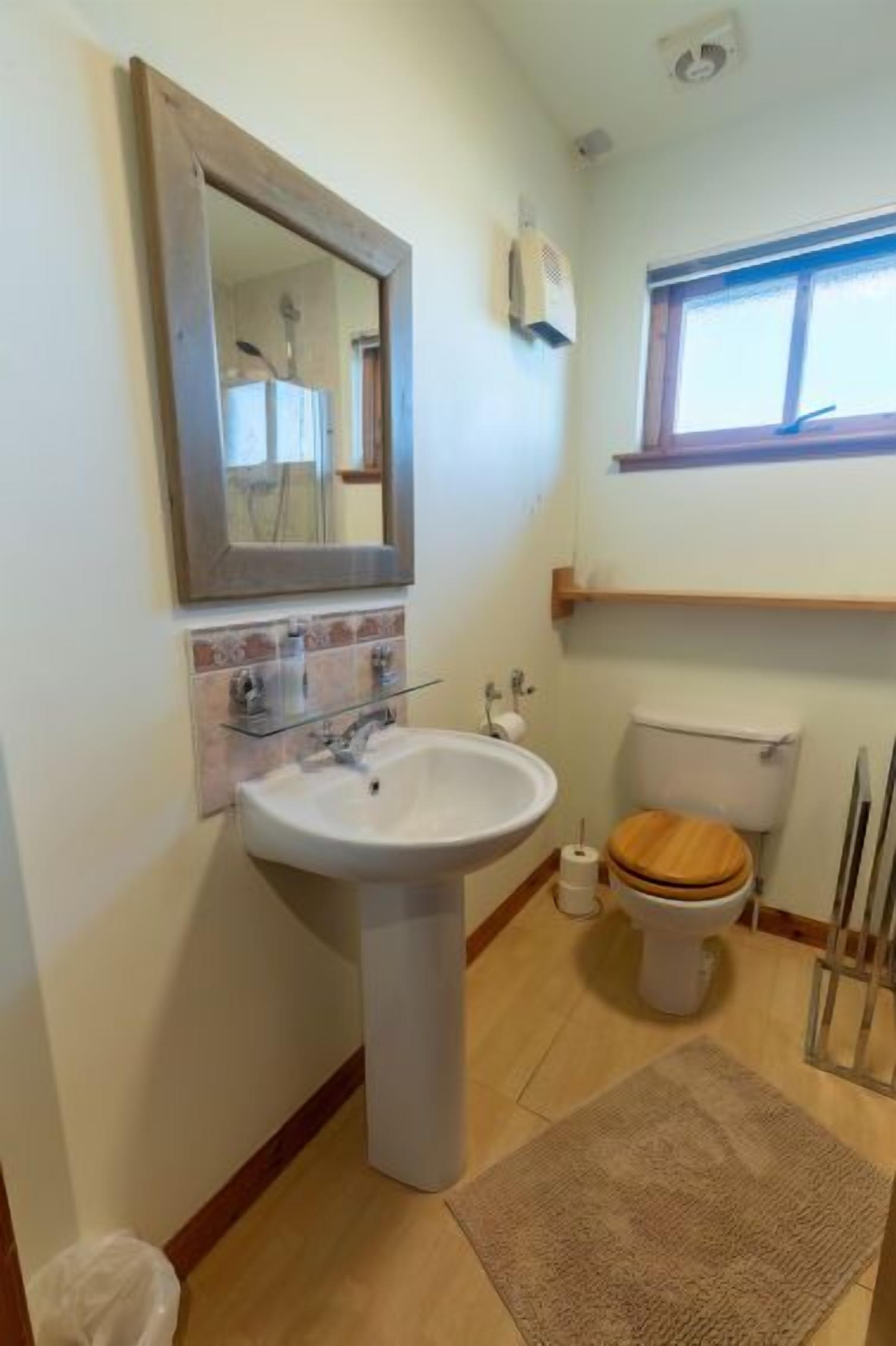 Ein Badezimmer mit einem Standwaschbecken, einer Toilette, einem Spiegel und einem Fenster.