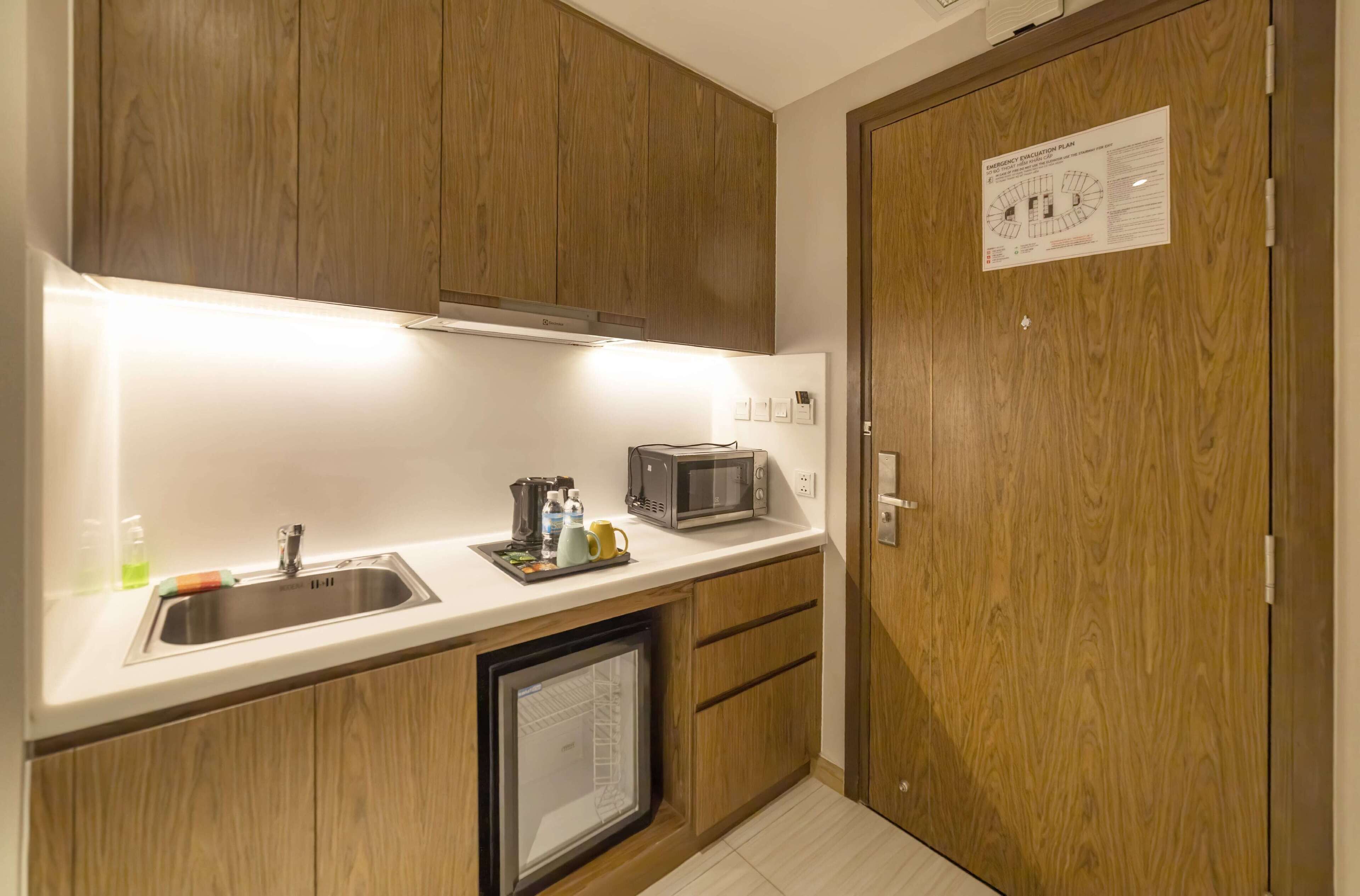 Une cuisine de taille réduite, dotée de meubles en bois, d’un four à micro-ondes, d’un évier et d’un réfrigérateur.