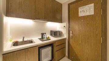 Une cuisine de taille réduite, dotée de meubles en bois, d’un four à micro-ondes, d’un évier et d’un réfrigérateur.