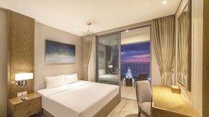 A modern hotel room with a large bed, a desk, and a view of the cityscape at dusk.