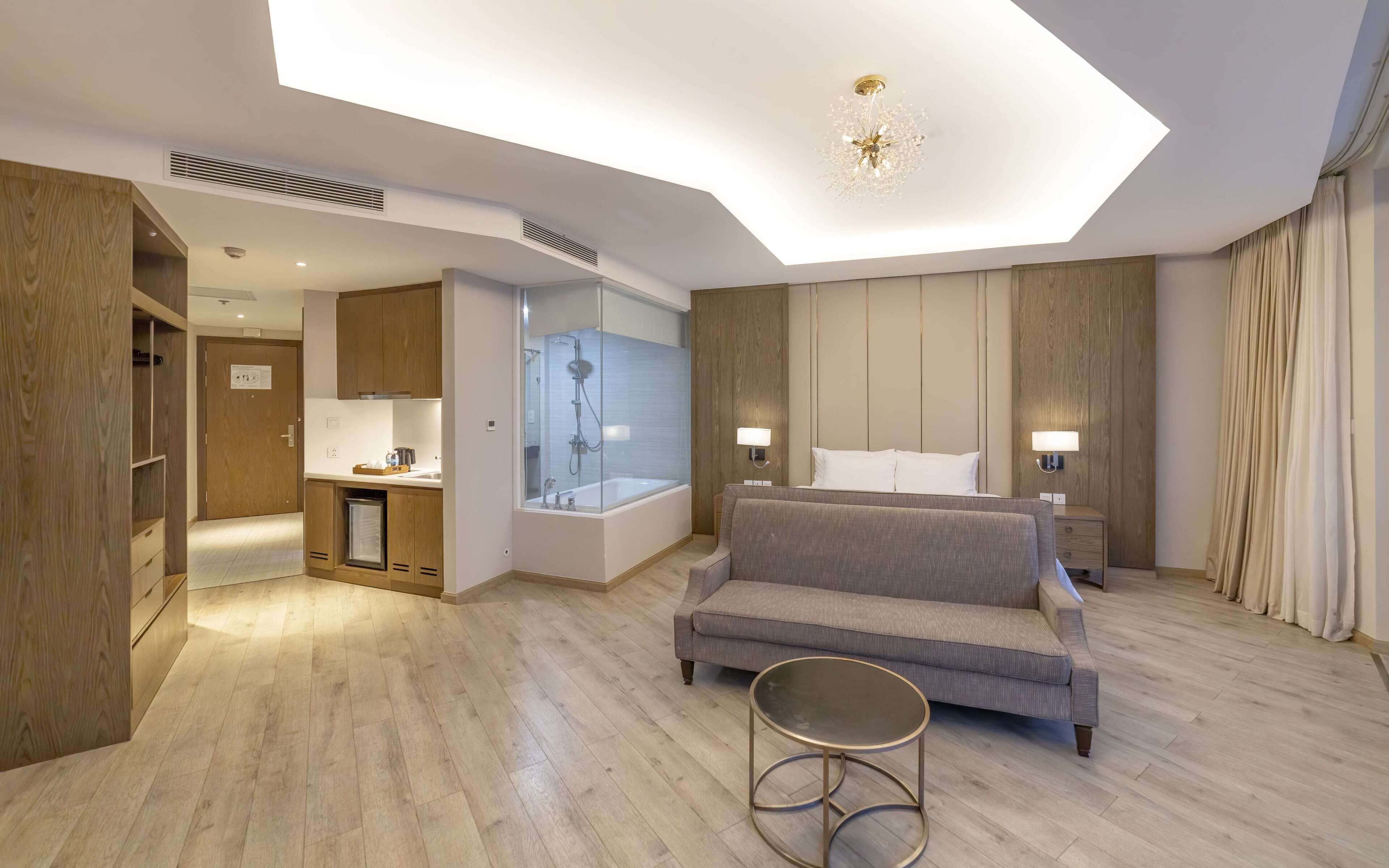 Habitación de hotel moderna con sofá, una mesa redonda, zona de ducha y armario de madera.