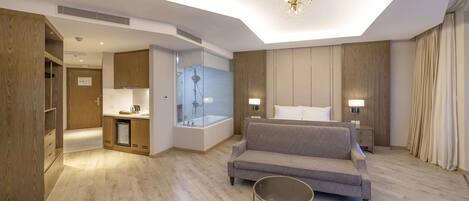 Habitación de hotel moderna con sofá, una mesa redonda, zona de ducha y armario de madera.