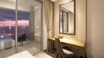 Una habitación de hotel moderna con un ventanal grande, un escritorio con silla, una mesita de noche y un espejo.