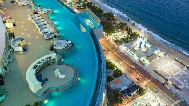 A rooftop pool area with sun loungers and a circular seating area, overlooking a beach and ocean.