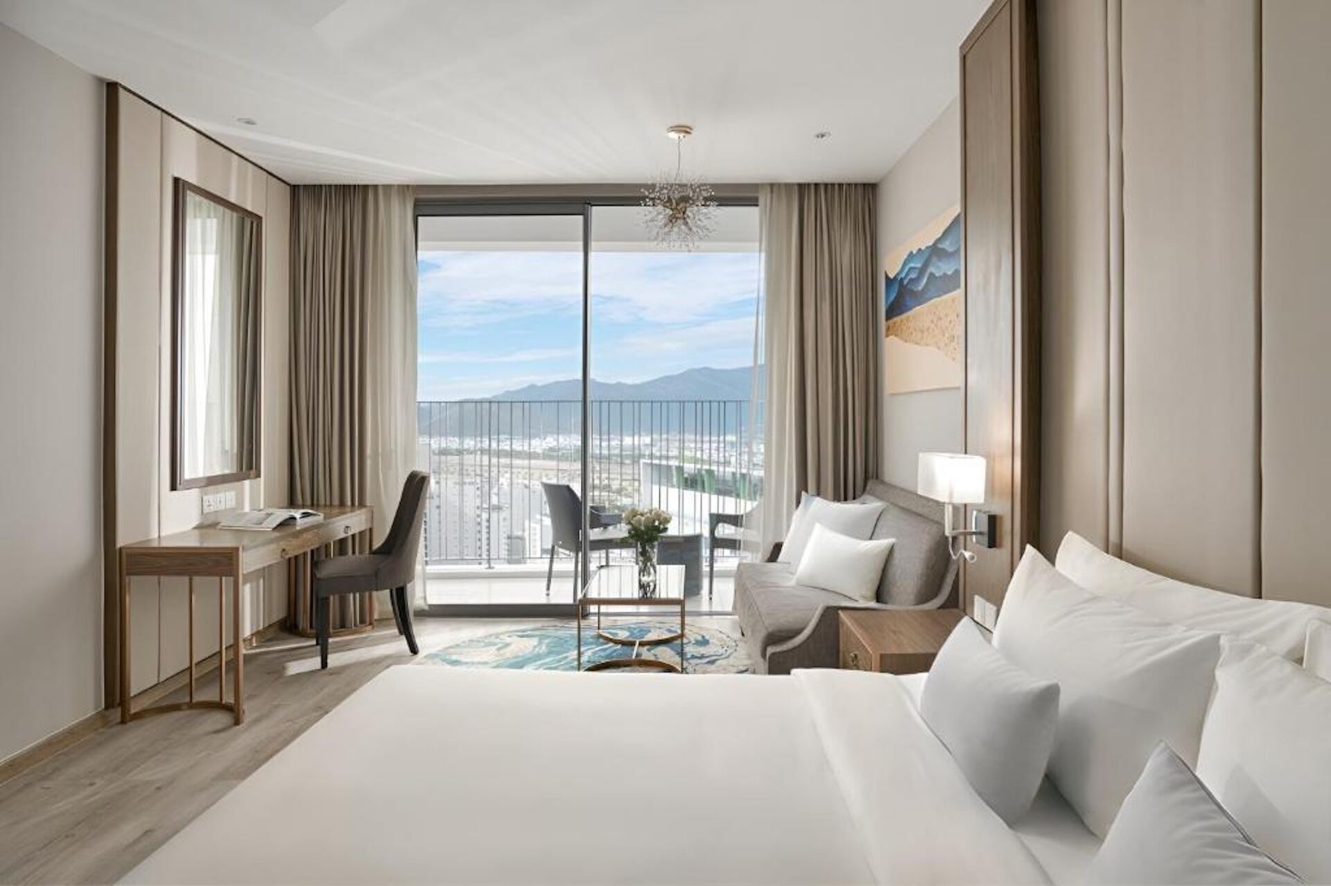 Habitación de hotel con una cama grande, un escritorio, una silla y vistas de la ciudad a través de las puertas del balcón.