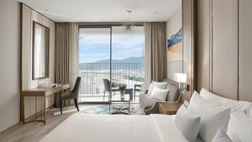 A hotel room with a large bed, a desk, a chair, and a view of the cityscape through the balcony doors.