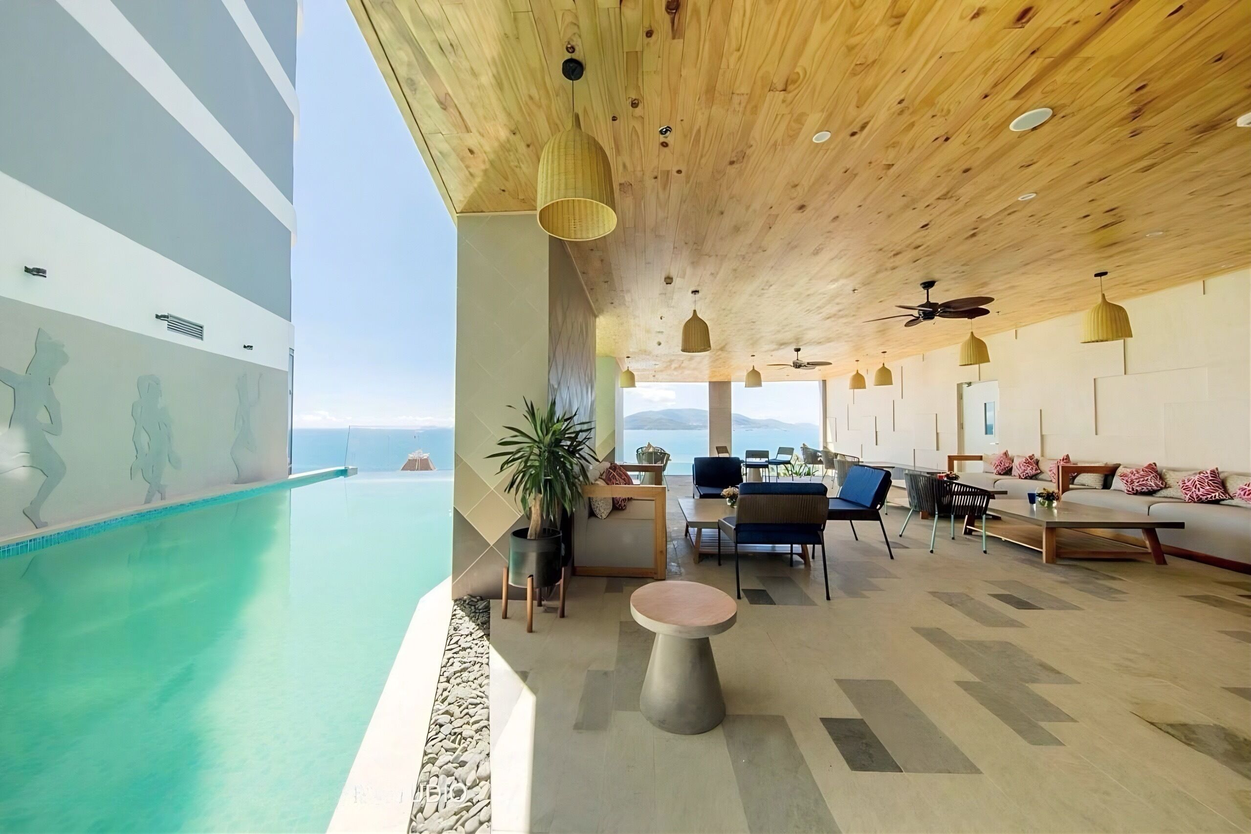 A modern indoor pool area with a wooden ceiling, seating, and a view of the ocean.