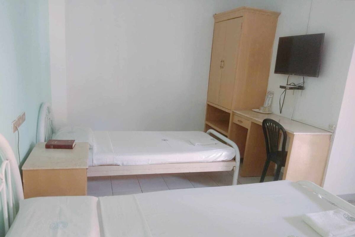 Habitació petita i senzilla amb un llit individual, una taula i una cadira.