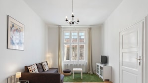 Una sala de estar moderna con un sofá, un televisor, una mesita y una ventana con cortinas.