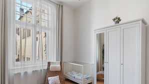 Una habitación con una cuna, una silla de mimbre, un armario y una ventana con cortinas traslúcidas.