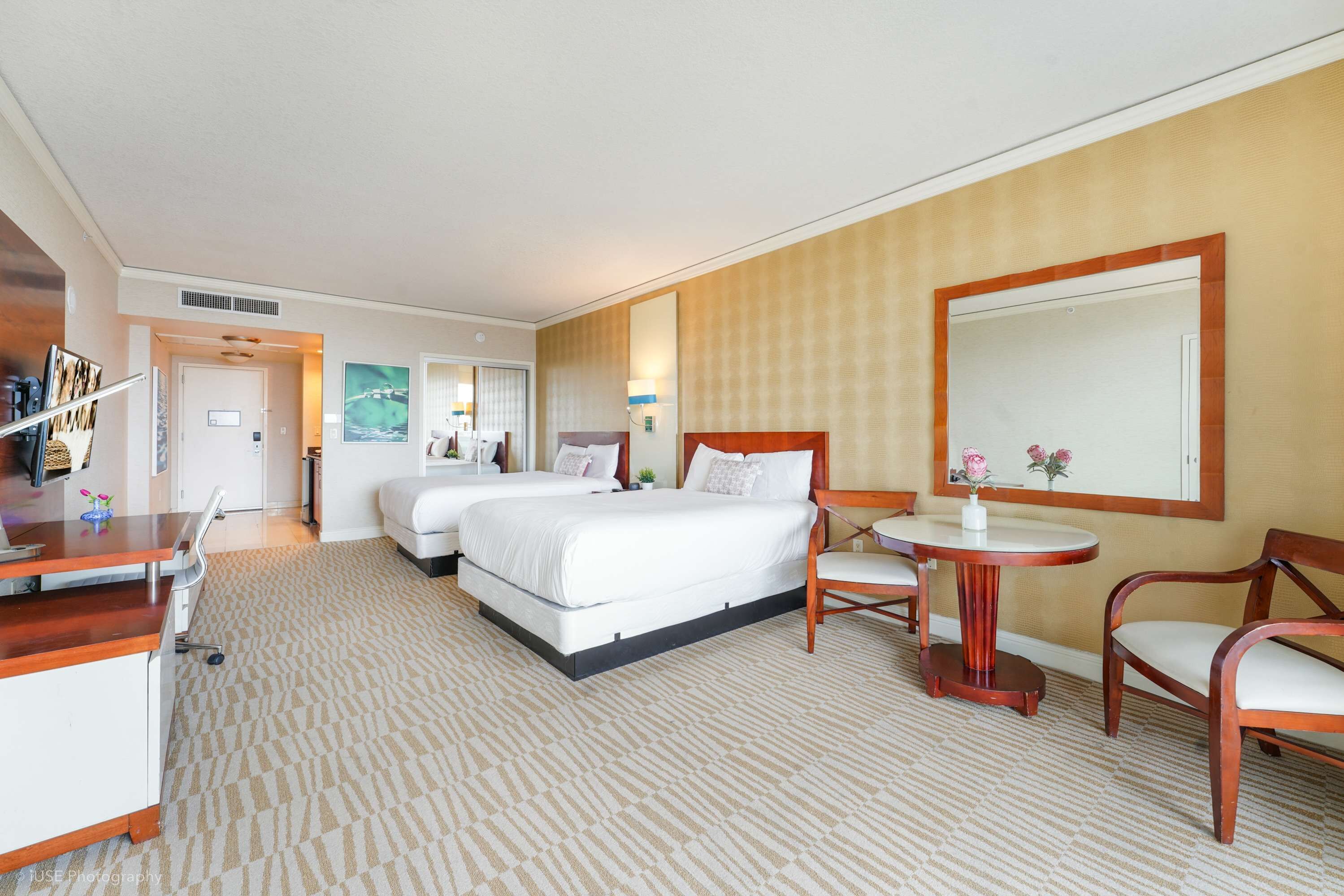 A hotel room with two beds, a desk, a chair, a small table, and a large mirror.