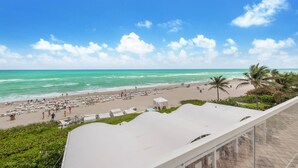 A beach with a clear sky, palm trees, and a white building with a roof.