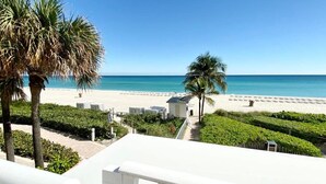 A balcony with a view of a beach, palm trees, and a clear blue sky.