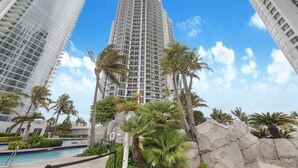 A high-rise hotel with a pool area, palm trees, and a clear blue sky.