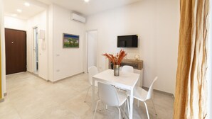 A modern dining area with a white table and chairs, a flat-screen TV mounted on the wall, and a painting on the wall. - Vico Cangiani al Mercato 20 (Naples)