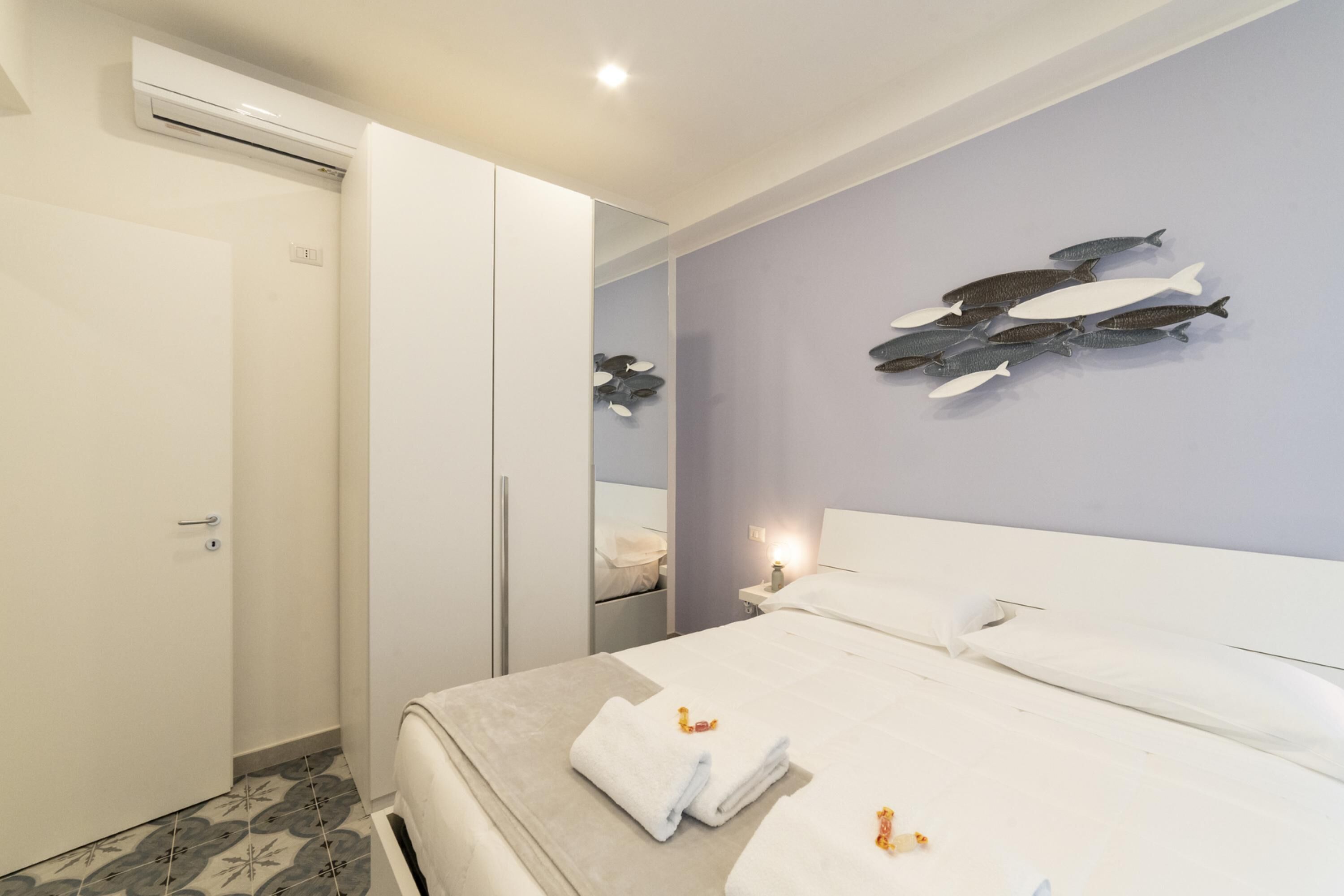 Una habitación de hotel moderna con una cama bien hecha, un espejo grande y una obra de arte de peces colgada en la pared.