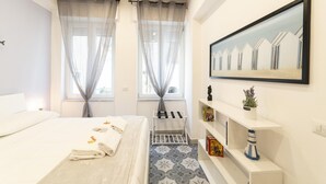 A modern hotel room with a large bed, two windows with sheer curtains, a small shelf with decorative items, and a framed picture on the wall. - Vico Cangiani al Mercato 20 (Naples)