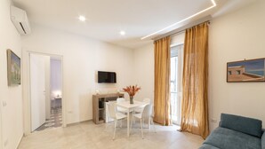 A modern living room with a sofa, a dining table with chairs, a TV mounted on the wall, and a window with curtains. - Vico Cangiani al Mercato 20 (Naples)
