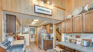 A kitchen with wooden cabinets, a stainless steel refrigerator, and a bar area with stools. - Sunriver Resort Home: Near Skiing, Town & Trails (Sunriver)