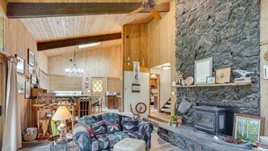 A cozy cabin interior with a stone fireplace, wooden walls, a dining area, and a living room with a patterned sofa and ottoman. - Sunriver Resort Home: Near Skiing, Town & Trails (Sunriver)