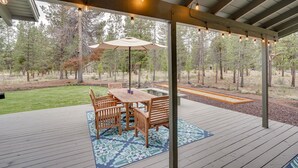 A covered outdoor patio with a wooden table and chairs, surrounded by a patterned rug. - Sunriver Resort Home: Near Skiing, Town & Trails (Sunriver)