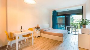 A modern bedroom with a bed, a desk, and a chair. There is a balcony with a view of greenery. - Mono Garden by Interhome (Marina di Bibbona)