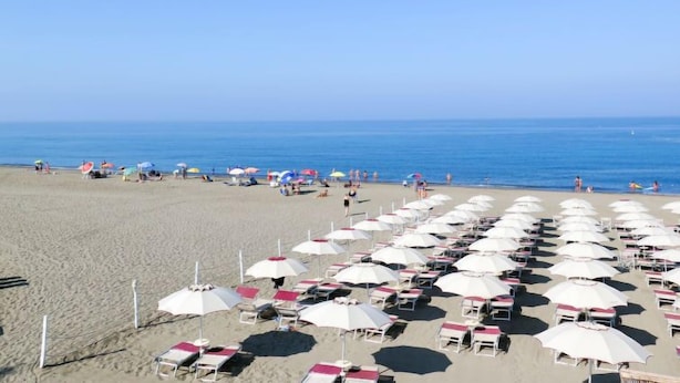 A beach with rows of white sunbeds and umbrellas, a clear sky, and the ocean in the background. - Bilo Plus Garden by Interhome (Marina di Bibbona)