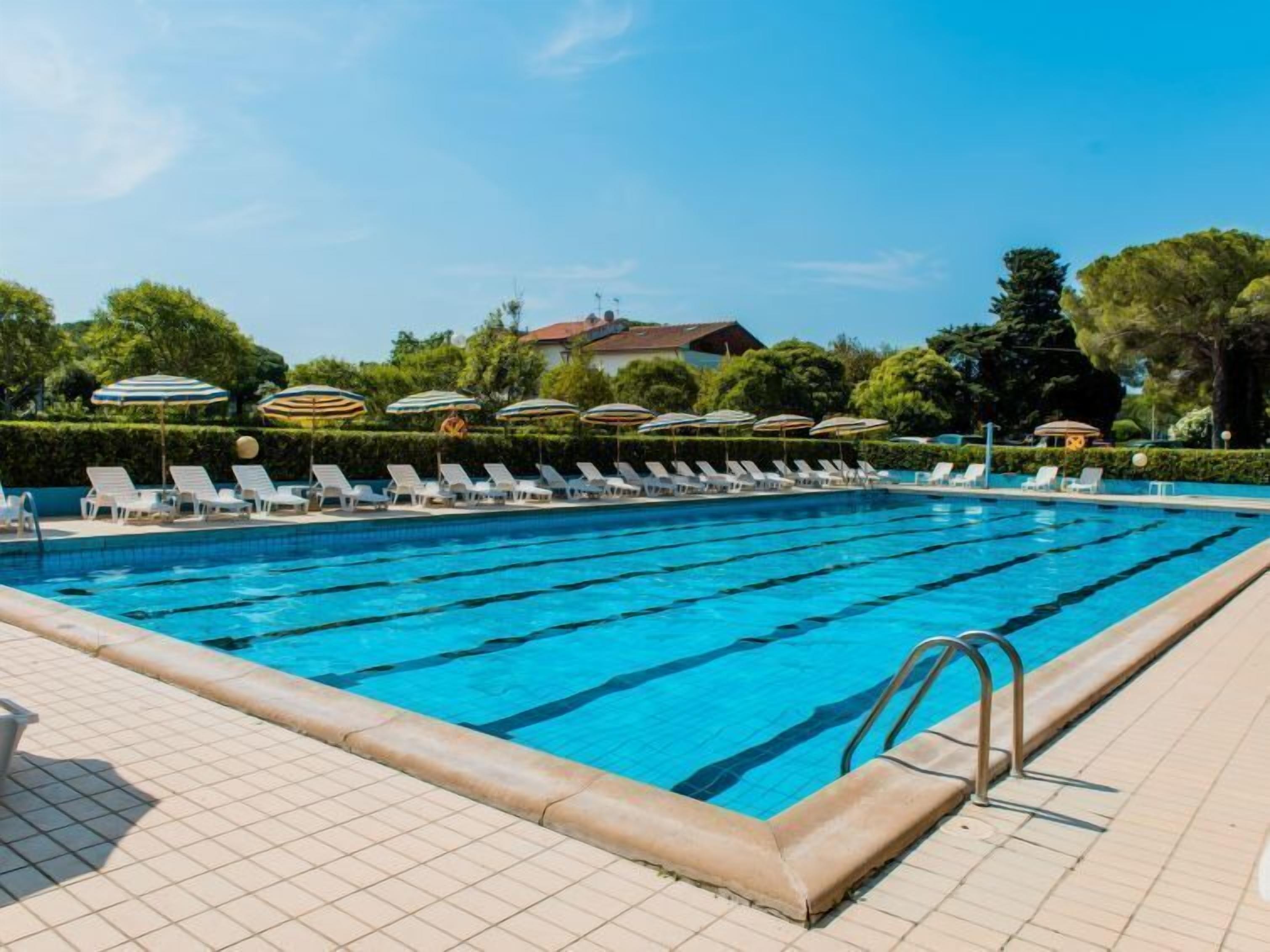 Ein Schwimmbecken mit mehreren Bahnen, Liegestühlen und Sonnenschirmen.