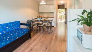 A compact living space with a sofa, dining table, chairs, a refrigerator, and a potted plant. - Bilo Standard Garden by Interhome (Marina di Bibbona)