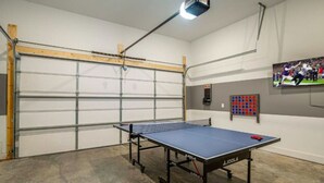 Et bordtennisbord i et rum med en garageport, et fjernsyn monteret på væggen og en pointtavle.