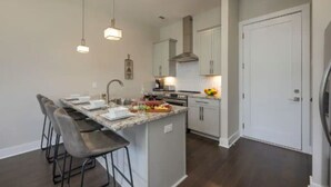 A modern kitchen with a central island, bar stools, pendant lighting, and white cabinetry. - Luxury Home w/ Rooftop & 8 Beds! 10 to Downtown! (Nashville)