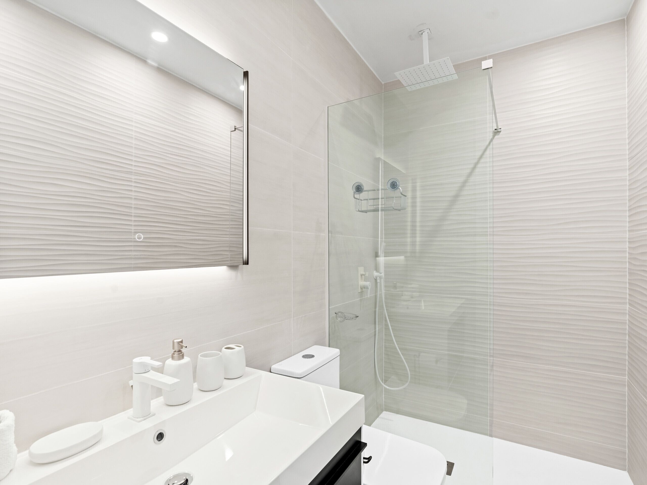 Een moderne badkamer met een douchecabine van glas, een witte wastafel en een toilet.