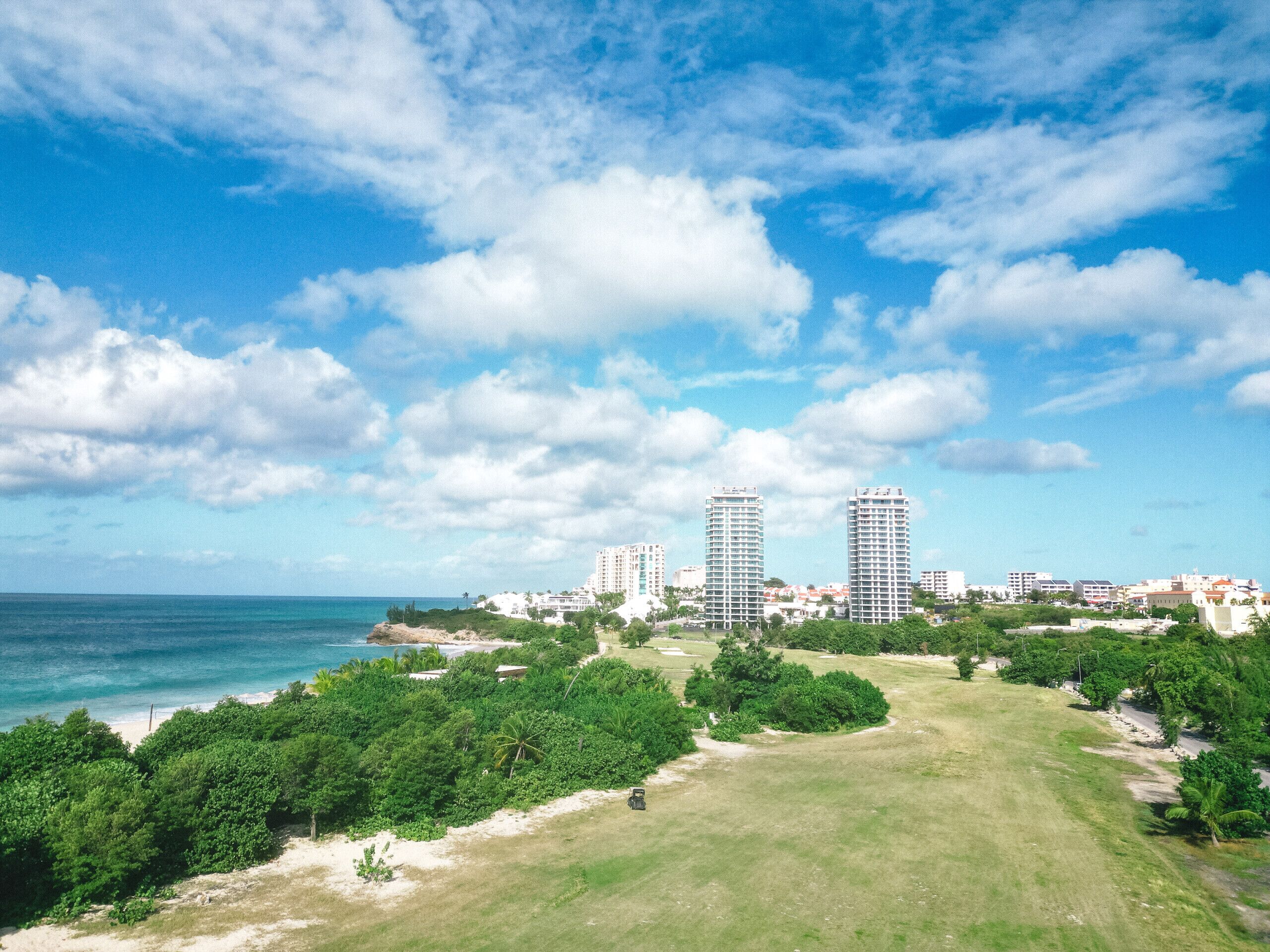 A coastal cityscape with two prominent high-rise buildings, a beach, and lush greenery.