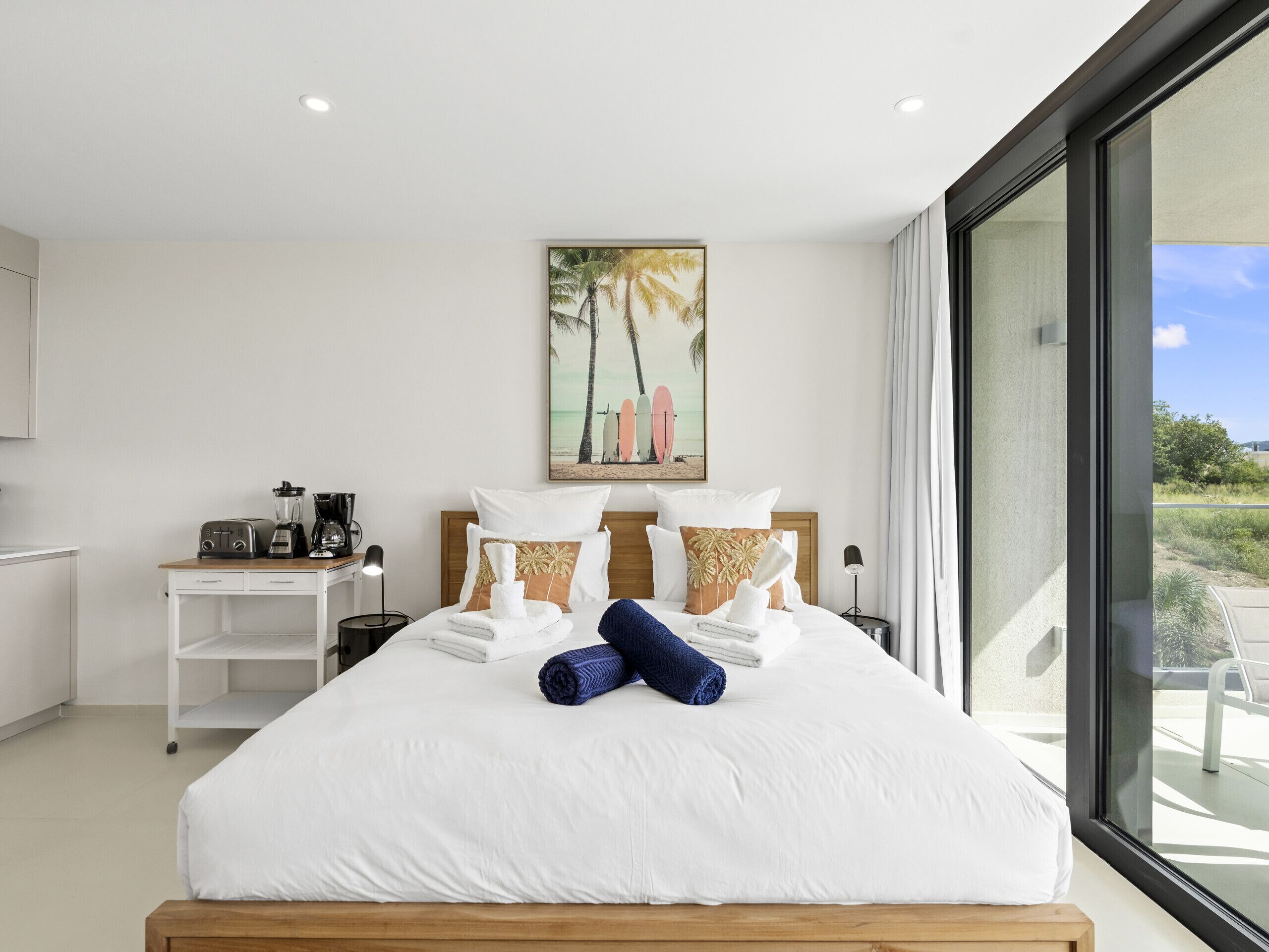 Une chambre d’hôtel moderne avec un grand lit, un petit bureau doté d’une machine à café et un tableau représentant une scène de plage.