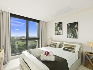 A modern hotel room with a large bed, a view of a golf course, and two wall art pieces. - B-904 Panoramic ocean view 1 bedroom cond (Cupecoy)