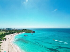 A coastal beach with clear turquoise waters, a sandy shore, and a few boats. - B-904 Panoramic ocean view 1 bedroom cond (Cupecoy)