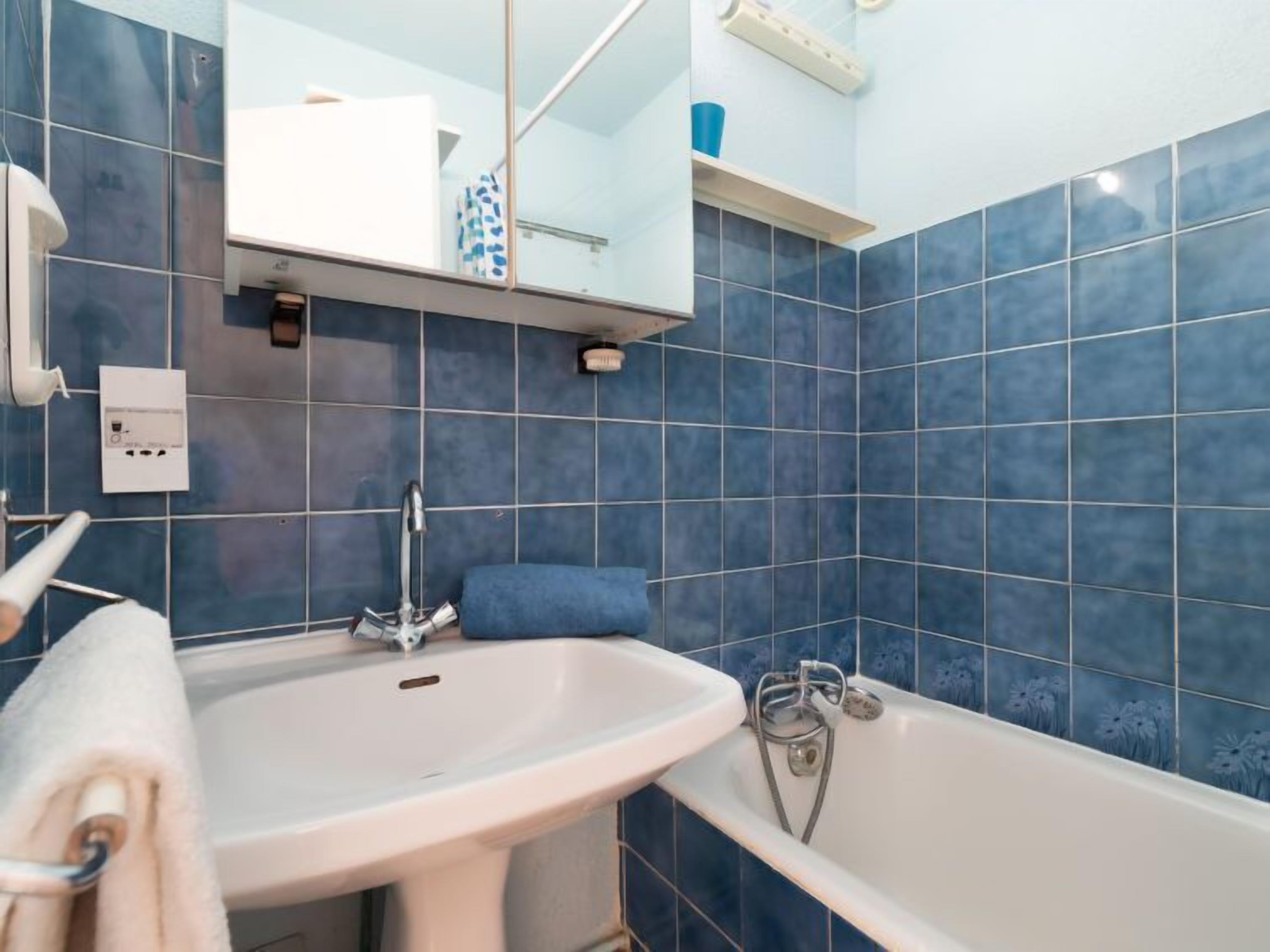 Un baño con lavamanos blanco, bañera y paredes con azulejos azules.