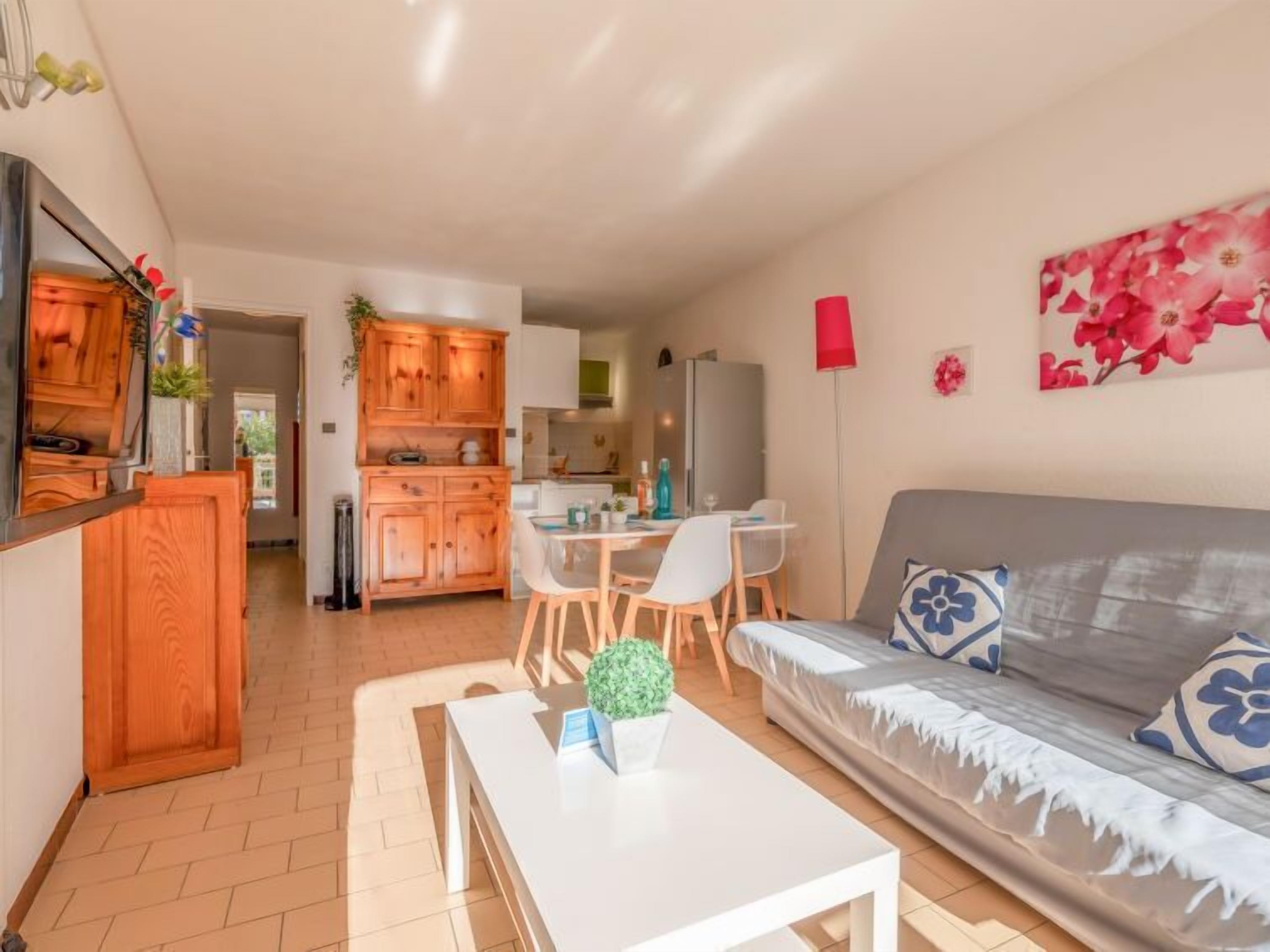 Un espace de vie compact comprenant un coin cuisine, un coin repas et un canapé agrémenté de coussins à motifs floraux.