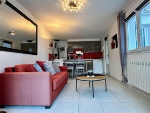 A compact living space with a red sofa, a small round table, and a kitchenette in the background. - Joannie by Interhome (Saint Brevin les Pins)