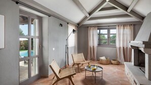 A spacious room with a large sliding glass door leading to a pool, a stone fireplace, and two wicker chairs around a small round table. - Rorripa by Interhome (Poreč/Sv. Lovreč)