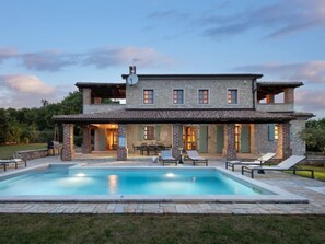 Une maison en pierre à deux étages, dotée d’une piscine, d’un espace salon extérieur et d’un patio couvert.