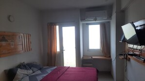 A bedroom with a bed, a desk, an air conditioner, and a TV. - OYO Life 93140 Apartment Grand Sentraland By Fahri (Karawang)