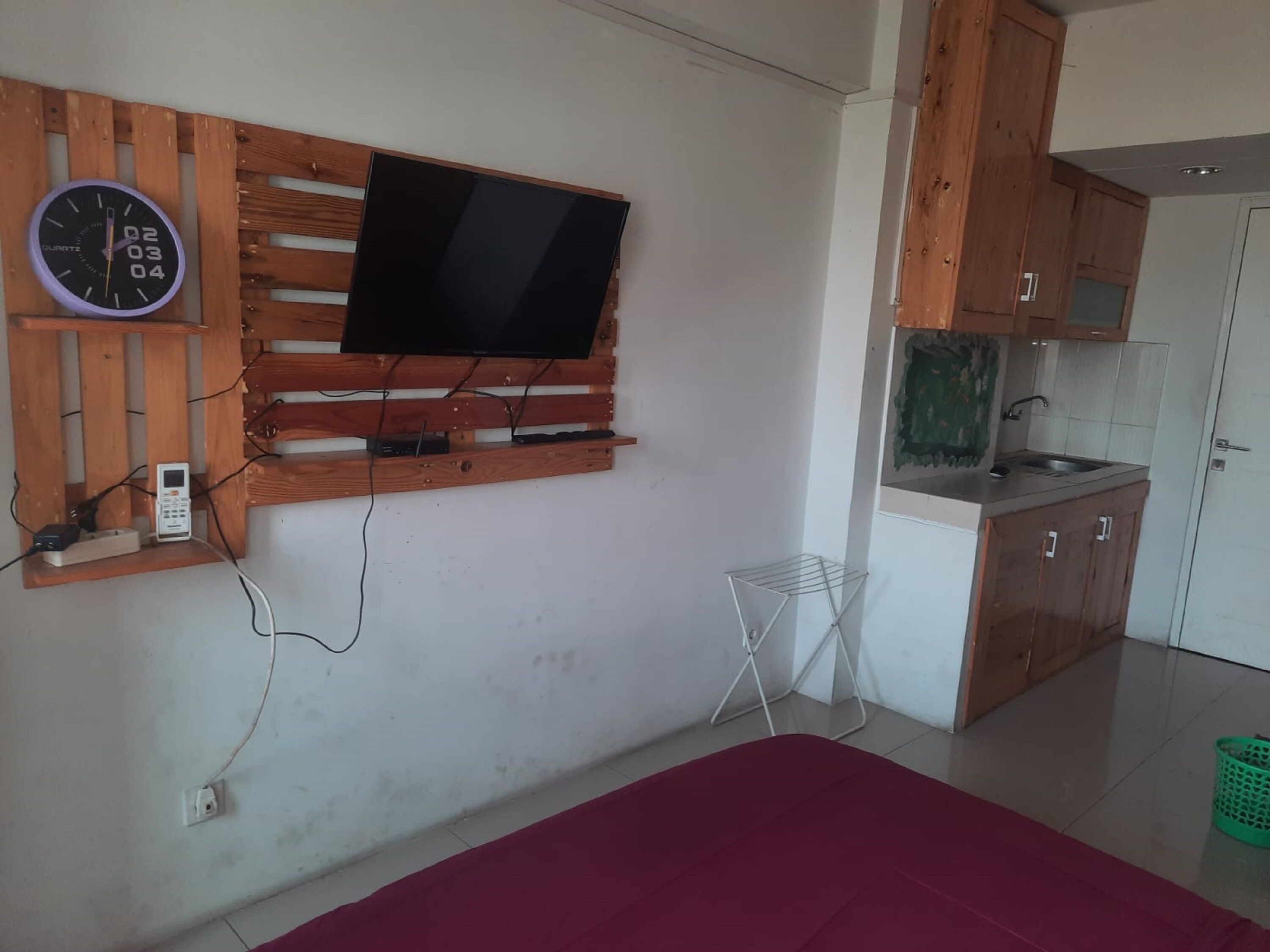 Een kamer met een wandtelevisie, een klok, een klein tafeltje en een kitchenette.